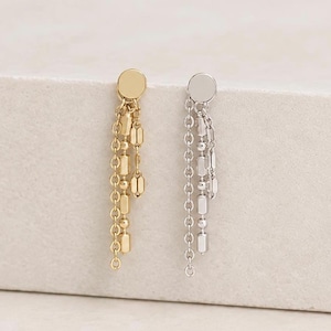 May include: A pair of drop earrings featuring a stud top with multiple dangling chains. One earring is gold-toned and the other is silver-toned. Each earring consists of a small circular stud connected to three delicate chains of varying lengths.