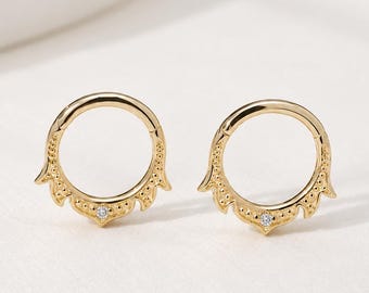 May include: A pair of gold hoop earrings featuring a circular design with a decorative scalloped edge and a small, clear, round-cut gemstone set at the base of each hoop. The metal has a polished finish with fine beaded detailing.