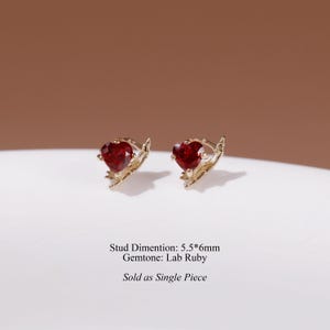 May include: Two gold stud earrings featuring heart-shaped lab ruby gemstones. The metal setting has a textured, branch-like design. Text on the image reads: Stud Dimention: 5.5*6mm Gemtone: Lab Ruby Sold as Single Piece.