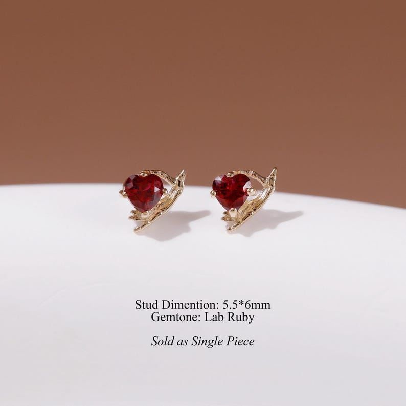 May include: Two gold stud earrings featuring heart-shaped lab ruby gemstones. The metal setting has a textured, branch-like design. Text on the image reads: Stud Dimention: 5.5*6mm Gemtone: Lab Ruby Sold as Single Piece.