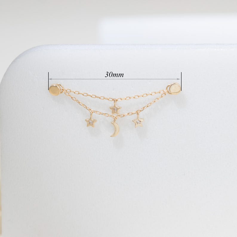 May include: A gold-toned double chain earring connector featuring two small star charms, one crescent moon charm, and two circular end posts. The piece measures 30mm in total length as indicated by the measurement lines visible in the image.