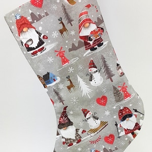 May include: A Christmas stocking with a gray background featuring a repeating pattern of gnomes, snowmen, snowflakes, and winter scenery. The gnomes are wearing red hats and coats. The stocking is approximately 18 inches long.