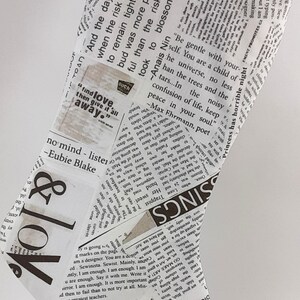 May include: A Christmas stocking with a newspaper print design. The white fabric is covered in black text and headlines. The stocking is hanging from a black metal stand. The text includes quotes and phrases.