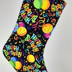 May include: Black stocking with a colorful pattern of balloons, confetti, and the words "Happy Birthday".