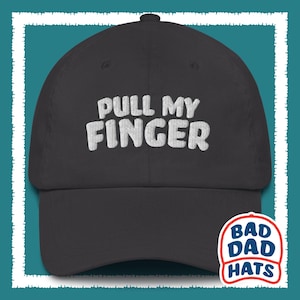 May include: A black baseball cap with white embroidered text that reads "PULL MY FINGER". The cap has a white logo on the back that reads "BAD DAD HATS".