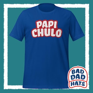 May include: Royal blue t-shirt with the words "PAPI CHULO" in white, outlined in red. The shirt features a crew neck and short sleeves. A "Bad Dad Hats" logo is visible on the bottom right.