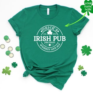 May include: Green t-shirt with a white circle design that says "Miller's Irish Pub est. 2023 Premium Whiskey and Ale".