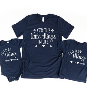 May include: Three navy blue t-shirts with white text. The largest shirt says "It's the little things in life" with arrows pointing to a heart. The two smaller shirts say "little thing" with an arrow pointing to a heart.