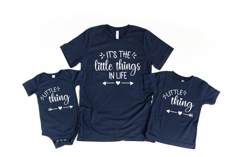 May include: Three navy blue t-shirts with white text. The largest shirt says "It's the little things in life" with arrows pointing to a heart. The two smaller shirts say "little thing" with an arrow pointing to a heart.