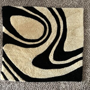 May include: A black and cream rug with a swirling, abstract pattern. The rug is made of a soft, plush material.