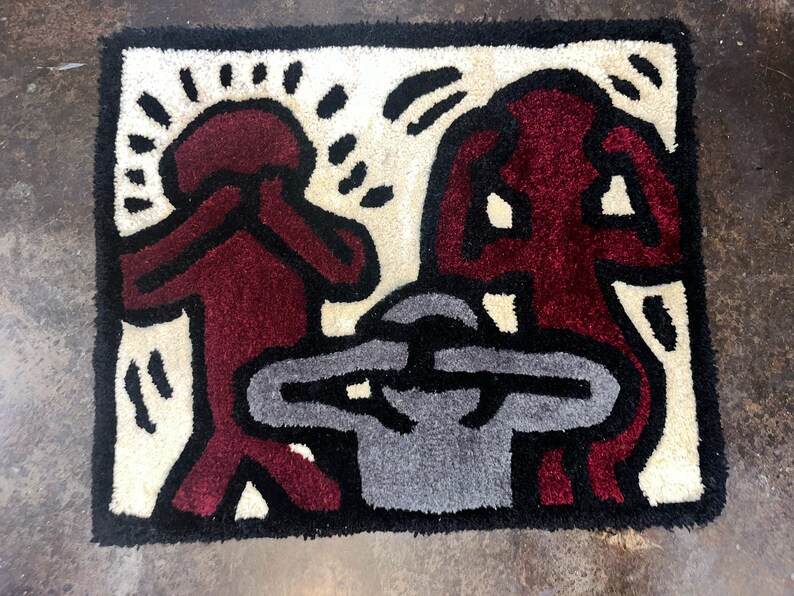 May include: A rug with a design of three figures, two in red and one in gray, with black outlines. The figures are stylized and have their hands covering their eyes. The rug has a white background.