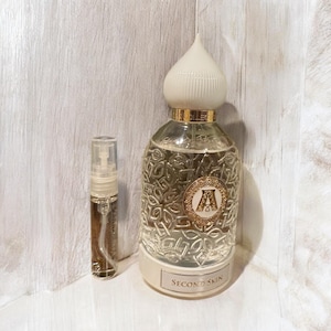 Puede incluir: Dos botellas de perfume, una grande y una pequeña. La botella grande es de vidrio transparente con una tapa dorada y un diseño dorado. La botella pequeña es de vidrio transparente con una tapa dorada. Ambas botellas tienen el texto "Second Skin" en la etiqueta.