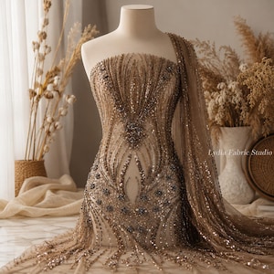 Puede incluir: Un maniquí exhibe una tela brillante con cuentas en tonos dorados y marrones. La tela está intrincadamente adornada con lentejuelas y cuentas, creando un patrón detallado. El diseño es adecuado para ropa formal o prendas de ocasión especial. La tela está drapeada.