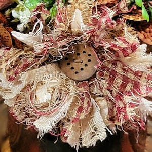 May include: A close-up of a handmade fabric flower with a brown metal button in the center. The flower is made of white and red fabric with a frayed edge.