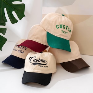 Pode incluir: Uma coleção de bonés de beisebol bege com abas coloridas. Alguns bonés têm texto bordado em verde, preto e azul marinho. Um boné diz "Custom Your Text" em uma fonte cursiva. Outro diz "Varsity Social Club".