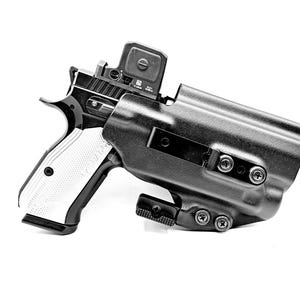 May include: A black handgun with a white grip is holstered in a black polymer holster. The holster has a red dot sight mounted on top of the gun. The holster has a belt clip and multiple screws.