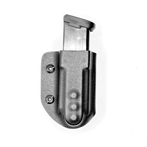 May include: A black plastic magazine holder with a black magazine inside. The holder has a textured surface and two screws on the side.