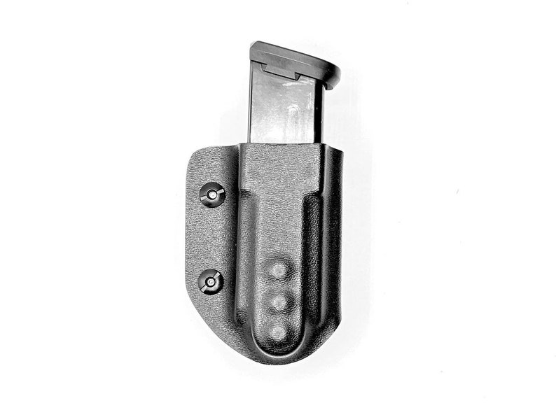 May include: A black plastic magazine holder with a black magazine inside. The holder has a textured surface and two screws on the side.