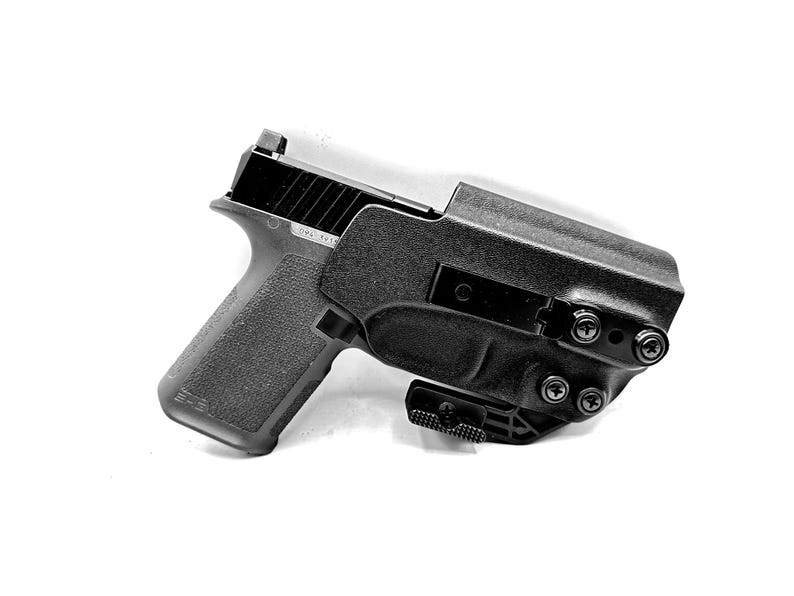 Puede incluir: Una pistola negra con una funda negra. La funda tiene un clip de metal y est&aacute; asegurada con tornillos.