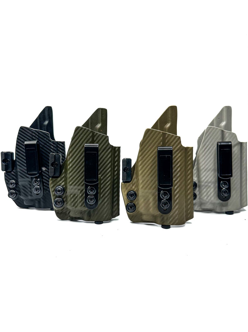 May include: Four different coloured holsters for concealed carry. The holsters are made of a carbon fibre material and have a black clip. The holsters are in a row from left to right: black, green, brown, and grey.