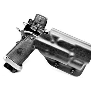 May include: A black handgun with a red dot sight in a black holster. The holster has a textured surface and is secured with screws.