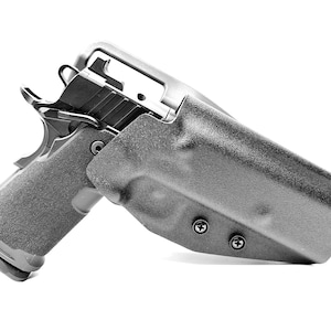 May include: A black and gray handgun is partially inserted into a matching holster. The handgun has a textured grip and a silver trigger. The holster is secured with two screws and has a molded shape.