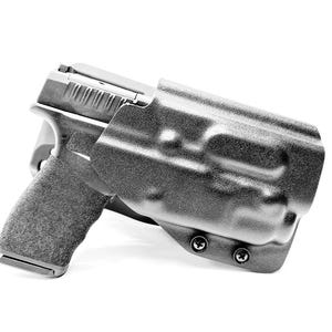 May include: A black handgun in a black holster. The handgun has a textured grip and a slide with serrations. The holster is molded to the shape of the gun and has two visible screws.