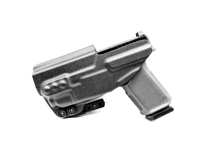 May include: A black polymer holster with a black handgun inside. The holster has a belt clip and a thumb release.
