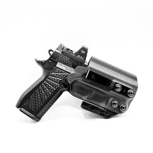 May include: A black handgun with a black holster. The gun has a textured grip and a red dot sight. The holster has a belt clip and multiple screws.