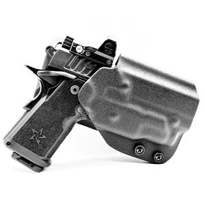 May include: A black and silver handgun with a red dot sight is holstered in a black holster. The handgun has a textured grip with a star emblem. The image is in black and white.
