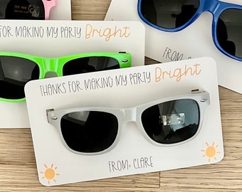 May include: Four thank you cards with sunglasses attached. Each card has the text "Thanks for making my party bright" and a small sun graphic. The cards are white with orange text and a different colored pair of sunglasses on each card: pink, green, blue, and gray.