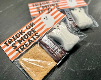 May include: A clear plastic bag filled with a s'more treat. The bag has a printed tag that says "Trick or S'more Treats" with orange and white stripes. The treat includes a graham cracker, a Hershey's milk chocolate bar, and a white marshmallow shaped like a ghost.
