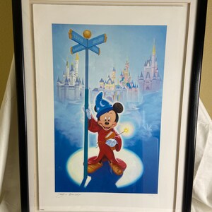 May include: Framed print featuring Mickey Mouse as a sorcerer, holding a wand and a book, standing before a signpost pointing to Tokyo, Orlando, Anaheim, and Paris. The artwork has a blue and white color scheme, with castles in the background.