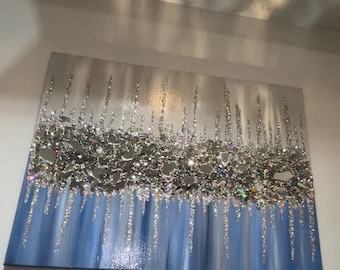 May include: Abstract wall art featuring a silver and blue color scheme. The artwork has a textured surface with silver glitter and reflective pieces. The bottom portion of the canvas is painted in shades of blue.