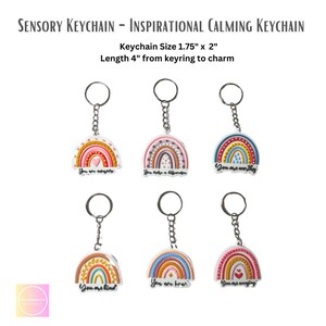 Op de afbeelding: Set van zes kleurrijke regenboogvormige sleutelhangers met inspirerende boodschappen. Elke sleutelhanger is 1,75 inch bij 2 inch en heeft een ketting van 4 inch. De boodschappen op de sleutelhangers zijn "You are worthy", "You make a difference", "You are an expert", "You are kind", "You are brave", en "You are amazing".