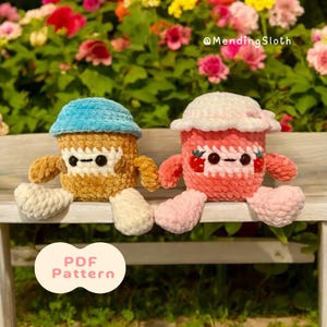 Peut inclure: Deux jouets en peluche crochetés en forme de pots de yaourt, l'un bleu et l'autre rose, assis sur un banc en bois. Le pot bleu a un visage blanc avec des yeux noirs et une bouche brune. Le pot rose a un visage blanc avec des yeux noirs et une bouche rouge. Le pot rose a une fraise rouge sur le dessus. Le texte "PDF Pattern" est sur un cercle de couleur pêche dans le coin inférieur gauche de l'image. Le texte "@MendingSloth" est dans le coin supérieur droit de l'image.