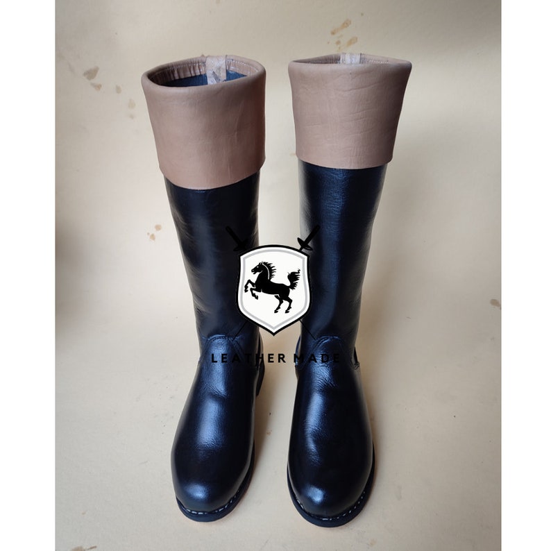 May include: A pair of black leather knee-high boots with brown leather tops. The boots have a rounded toe and a low heel.
