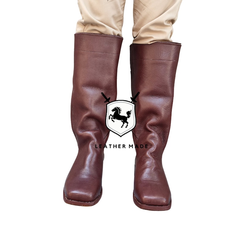K&ouml;nnte beinhalten: Ein Paar braune, kniehohe Lederstiefel mit quadratischer Spitze. Die Stiefel sind aus glattem Leder gefertigt und haben ein schlichtes Design.