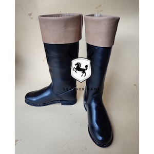 May include: A pair of black leather riding boots with brown leather tops. The boots have a simple design and a rounded toe.