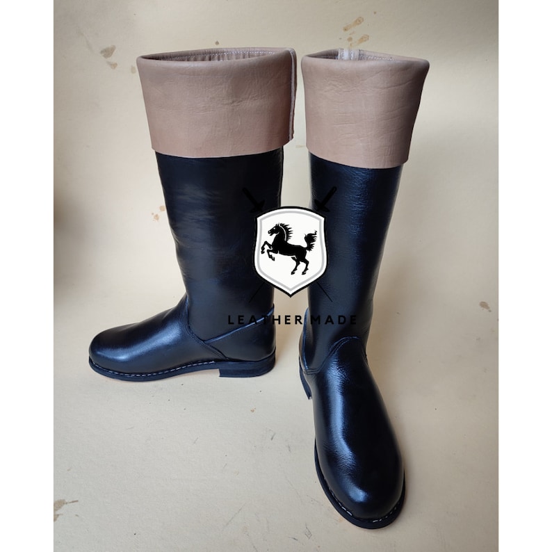 May include: A pair of black leather riding boots with brown leather tops. The boots have a simple design and a rounded toe.