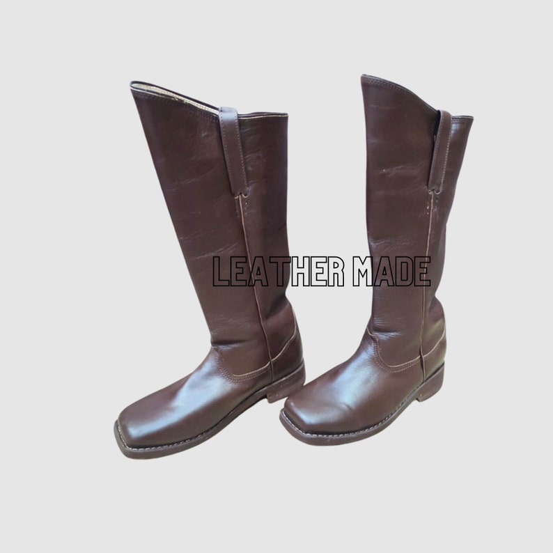 May include: A pair of dark brown leather knee-high boots with a square toe design, low heels, and vertical side pull tabs. The text LEATHER MADE is printed in black outlined capital letters between the two boots against a plain background.