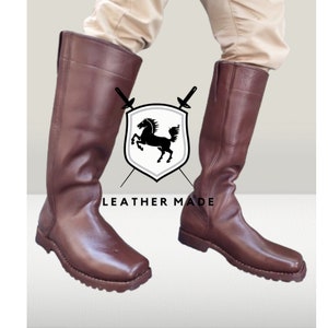K&ouml;nnte beinhalten: Ein Paar braune, kniehohe Lederstiefel mit quadratischer Spitze und dicker Sohle. Die Stiefel werden von Leather Made hergestellt.