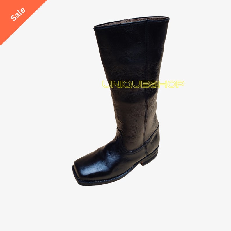 K&ouml;nnte beinhalten: Ein schwarzer Wadenstiefel aus Leder mit quadratischer Zehenpartie, niedrigem Absatz in Schichtoptik und sichtbaren N&auml;hten an der Sohle. Das Wort UNIQUESHOP ist in gelber Schrift auf dem Schaft des Stiefels mit strukturierter Oberfl&auml;che gedruckt.