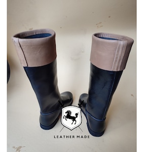 May include: A pair of black leather riding boots with brown leather tops. The boots have a simple design and a rounded toe.