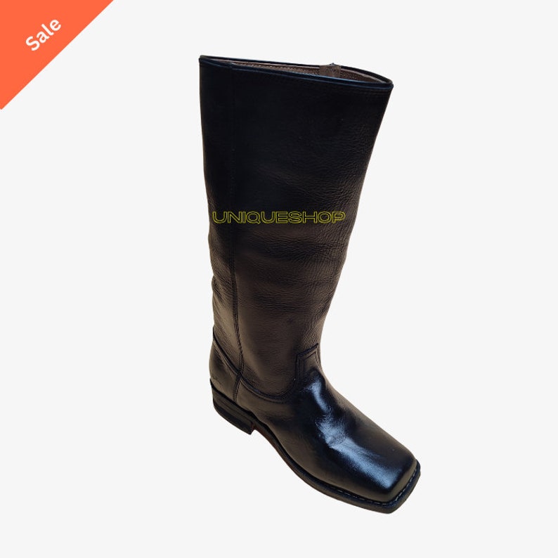 K&ouml;nnte beinhalten: Ein hoher schwarzer Lederstiefel mit quadratischer Zehenpartie und niedrigem Absatz. Der Stiefel hat einen strukturierten Schaft und einen glatten Lederfu&szlig;bereich mit sichtbaren N&auml;hten entlang der Sohle. Der Text UNIQUESHOP ist gelb aufgedruckt.