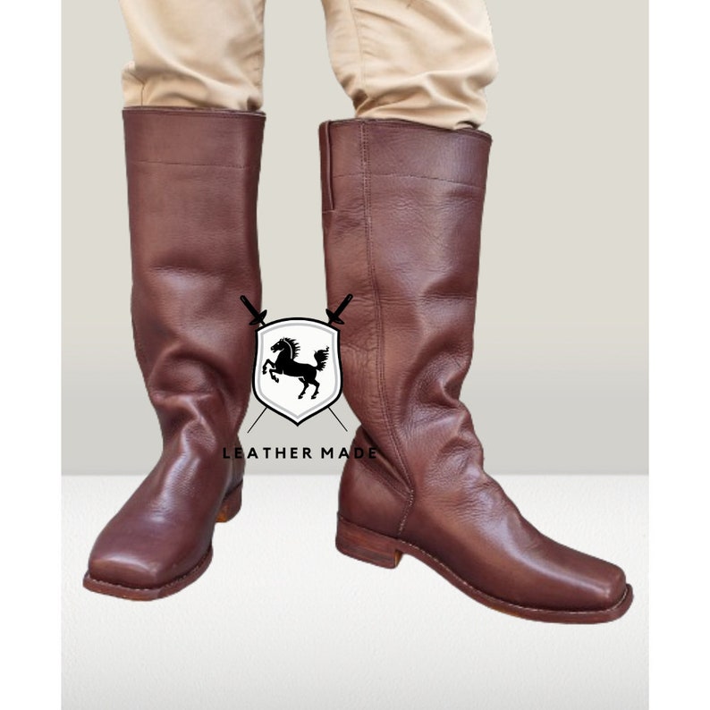 K&ouml;nnte beinhalten: Ein Paar braune, kniehohe Lederstiefel mit quadratischer Spitze. Die Stiefel haben ein schlichtes Design und sind aus hochwertigem Leder gefertigt.
