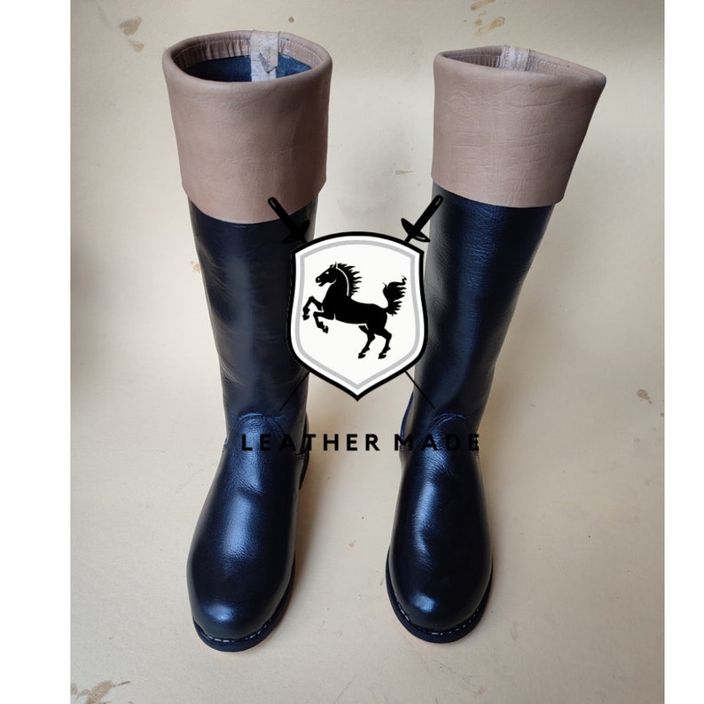 May include: A pair of black leather riding boots with brown leather tops. The boots have a classic design and are made of high-quality leather.