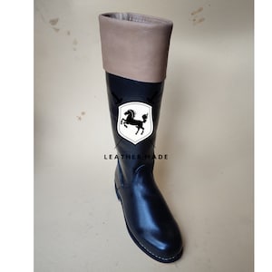 May include: Black leather riding boots with a brown leather cuff. The boots have a pointed toe and a low heel. The boots are made by LEATHER MADE.