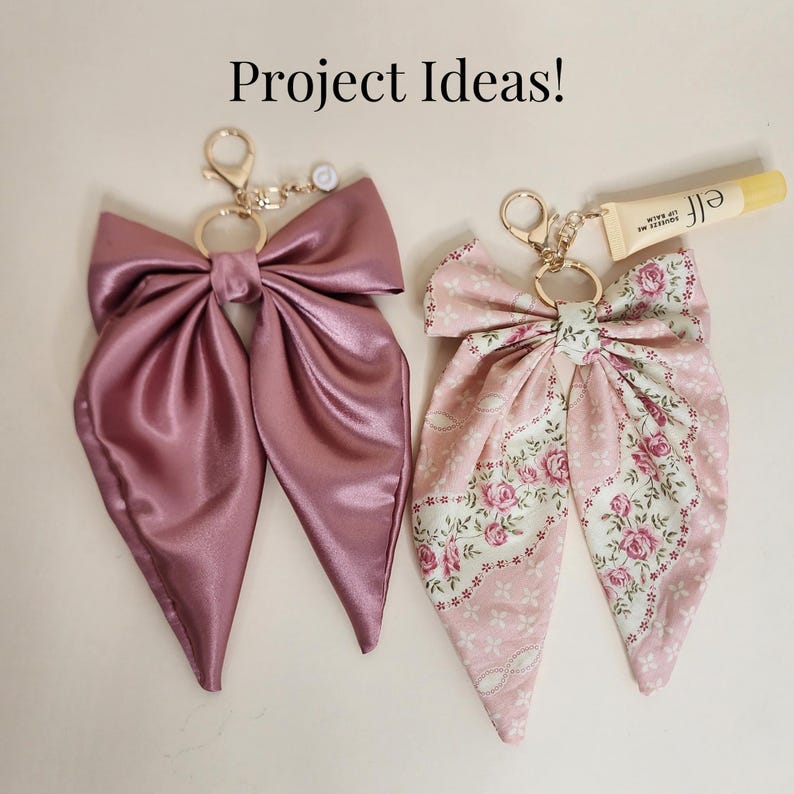 May include: Two decorative bow keychains. One is a solid mauve satin, the other is a pink floral print. Both have gold-colored hardware and a small charm. The text "Project Ideas!" is at the top.