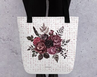 May include: A white tote bag with black handles features a watercolor floral design. The design includes dark pink and burgundy roses with green leaves and stems on a white background with a subtle pink grid pattern.